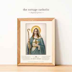 May include: A framed digital print featuring an illustration of St. Brigid of Kildare. The artwork depicts a woman in a blue cloak, holding a staff and a cross. The print includes the text "the cottage catholic - digital print -" and additional text at the bottom.