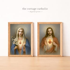 May include: Two framed prints featuring religious figures. One depicts a woman in a blue robe holding flowers, the other a man in a red robe. Both have a glowing heart and a halo. The text "the cottage catholic - digital print -" is at the top.