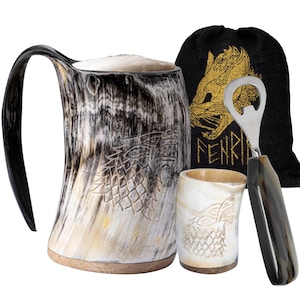 May include: A Viking-themed drinking set. It includes a large horn mug, a small cup, a bottle opener, and a black bag with a gold wolf design. The mug and cup have carved wolf designs. The set is made of natural materials.