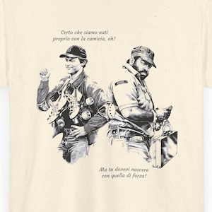 Può includere: T-shirt color crema con un'illustrazione in bianco e nero di due uomini. L'illustrazione include testo in italiano. La maglietta ha un girocollo classico e maniche corte, adatta per l'abbigliamento casual.