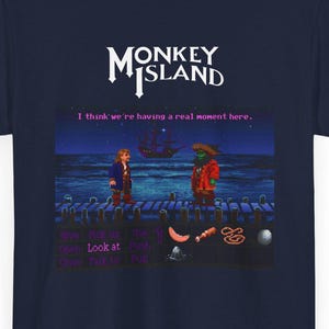 May include: Navy blue t-shirt with a Monkey Island video game graphic. The design shows the game's logo and a scene with two characters on a pier, with the text "I think we're having a real moment here."