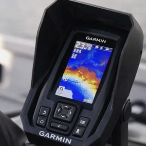 Può includere: Un ecoscandaglio Garmin montato su una barca. Lo schermo mostra una vista subacquea colorata con profondità e altri dati. Il dispositivo ha diversi pulsanti e un cappuccio protettivo. Il logo Garmin è visibile.