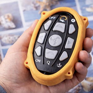 Puede incluir: Un mando a distancia amarillo y negro con varios botones, incluyendo "OFF" y "ON". El mando tiene un icono de ventilador y un icono de ancla. El mando se sostiene en una mano.