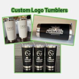 May include: A collection of custom logo tumblers in various designs. Some tumblers are white with the "EAGLE Dental" logo, while others are black with logos for "Murf Turf Sprinklers" and "Trivia Night Champion". All tumblers have a silver base and rim.