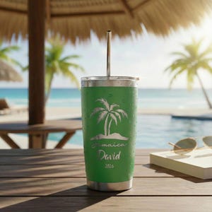 May include: A green travel tumbler with a silver lid and straw. The tumbler features a palm tree design with the word "Jamaica" and the name "David" and the year "2026". The tumbler is sitting on a wooden surface near a pool and beach.