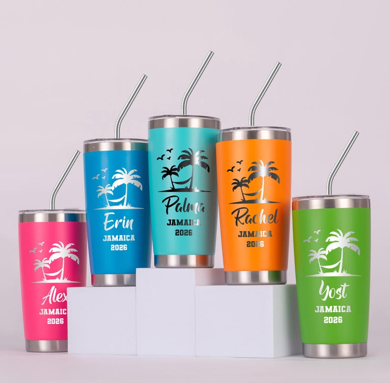 May include: Five brightly coloured stainless steel travel mugs with silver straws. Each mug has a name, palm tree design, and the text "Jamaica 2026". Colours include pink, blue, teal, orange, and green. The mugs are displayed on a white surface.