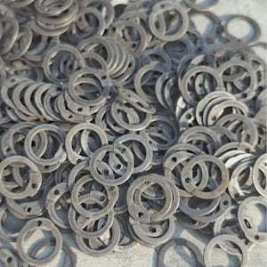 May include: A large collection of circular metal retaining rings, each featuring a small hole on one side. These industrial fasteners are grey in color with a matte finish, scattered in a dense pile to show their uniform shape and design.