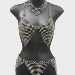 May include: A silver chainmail bikini set displayed on a mannequin. The set includes a halter top, a matching choker necklace, and a low-rise bottom. The chainmail is made of small, interlocking metal rings.