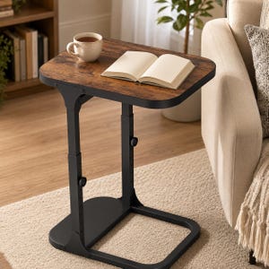 May include: A height-adjustable C-shaped side table with a dark brown wood-grain finish tabletop and a black metal frame. The table features two vertical support posts with adjustable knobs and a flat base, holding an open book and a ceramic mug.