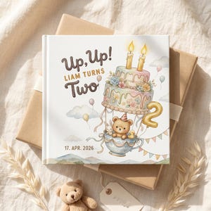 Puede incluir: Un libro de tapa dura cuadrado con cubierta blanca que presenta una ilustraci&oacute;n en acuarela de un osito de peluche, un conejo y un patito en un globo aerost&aacute;tico de taza de t&eacute;. Un pastel de pisos con dos velas est&aacute; encima. Texto: Up, Up! LIAM TURNS Two 17. APR. 2026.