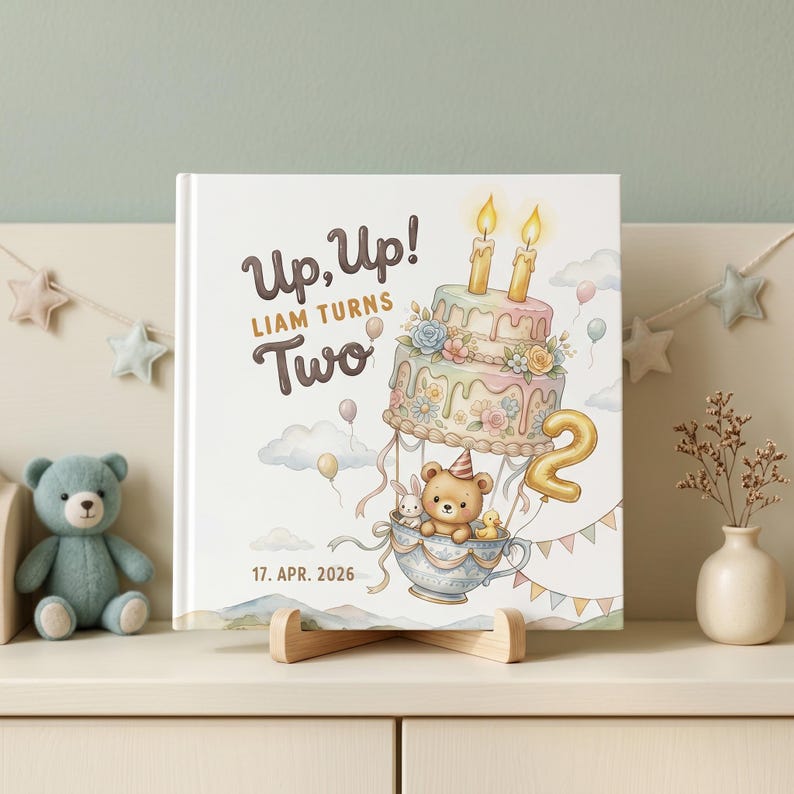 Puede incluir: Una portada de libro cuadrada con un pastel de varios niveles en tonos pastel que flota como un globo aerost&aacute;tico, llevando un oso de peluche, un conejo y un pato en una taza de t&eacute;. El texto dice Up, Up! LIAM TURNS Two y 17. APR. 2026.