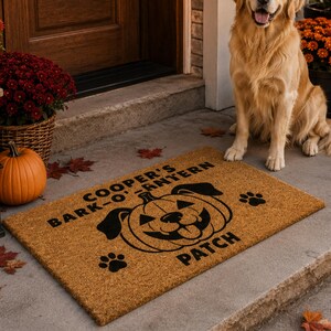 May include: A rectangular tan coir doormat featuring a black graphic of a dog face inside a carved pumpkin. The text reads COOPER'S BARK-O'-LANTERN PATCH, accompanied by two black paw prints. The mat is positioned on a concrete porch floor.