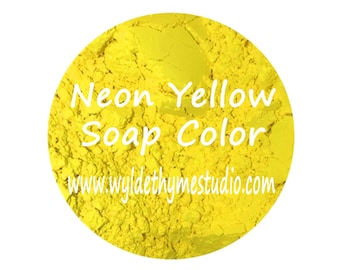 May include: A close-up of a bright yellow powder labeled "Neon Yellow Soap Color" with the website www.wyldethyme studio.com printed below. The powder is in a round container with a white background. The text "AURORA DYZ" is printed below the container.