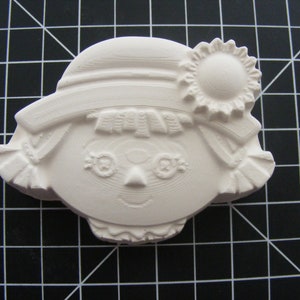 May include: White ceramic figurine of a girl with a hat and a flower. The girl has a simple face with eyes, a nose, and a smile. The figurine is a blank canvas for painting.