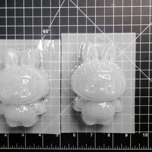 Puede incluir: Dos moldes transparentes con forma de conejito se muestran sobre una superficie de rejilla negra. Los moldes est&aacute;n hechos de un material transl&uacute;cido, con detalles como orejas, un cuerpo esponjoso y una cara bonita. Los moldes est&aacute;n en un embalaje de pl&aacute;stico transparente.