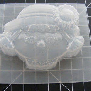 May include: Clear plastic mold for making a doll-shaped soap or candle. The mold features a girl with a hat and a flower on her head.