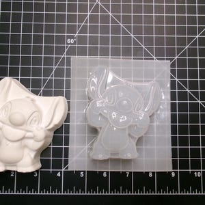 May include: A white, cast resin figure of the character Stitch from the Disney movie Lilo & Stitch, next to a clear silicone mold of the same character. The figure is approximately 3 inches tall.