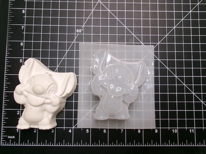 May include: A white, cast resin figure of the character Stitch from the Disney movie Lilo & Stitch, next to a clear silicone mold of the same character. The figure is approximately 3 inches tall.