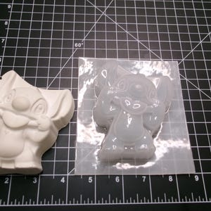 May include: A white, cast resin Stitch figurine and a clear silicone mold of Stitch. The figurine is a solid, three-dimensional form. The mold is filled with a clear, gel-like substance, showing Stitch's features.