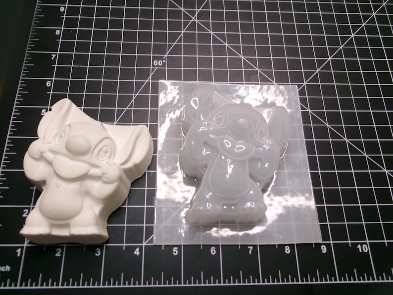 May include: A white, cast resin Stitch figurine and a clear silicone mold of Stitch. The figurine is a solid, three-dimensional form. The mold is filled with a clear, gel-like substance, showing Stitch's features.