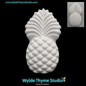 May include: White ceramic pineapple mold with a detailed design. The mold is shaped like a pineapple with a textured surface and a leafy top.