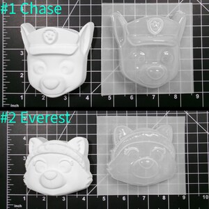 May include: Two clear plastic molds for making character figures. The molds are on a gridded surface. The first mold is of Chase from Paw Patrol, a white dog with a blue hat and a paw print badge. The second mold is of Everest from Paw Patrol, a white dog with a pink hat and a blue scarf. The molds are labeled #1 Chase and #2 Everest.