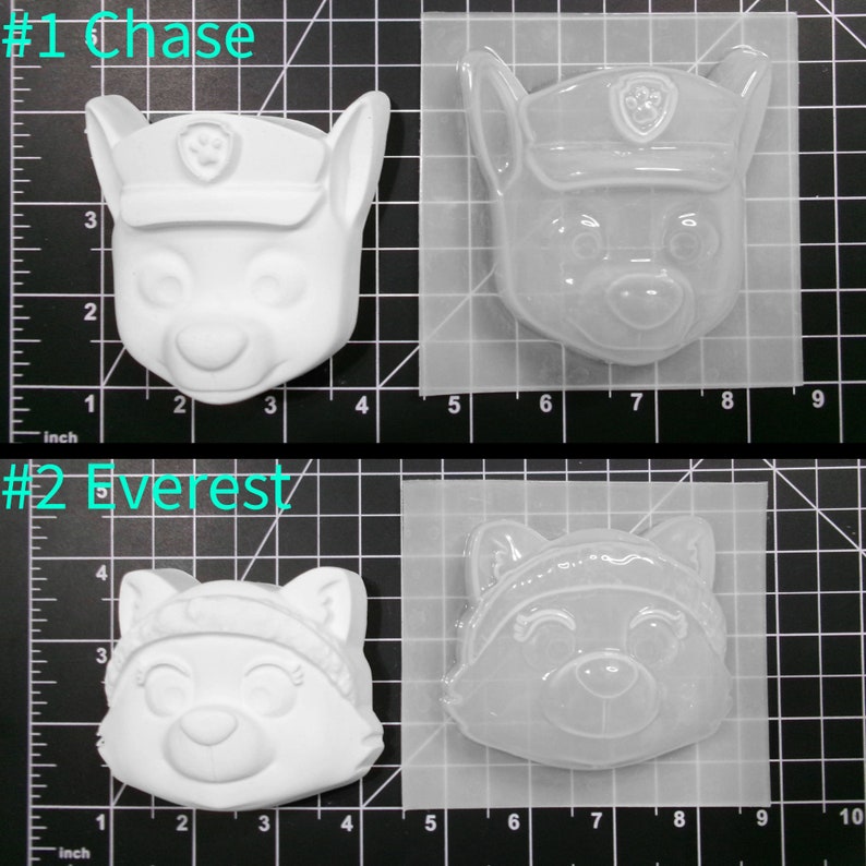 May include: Two clear plastic molds for making character figures. The molds are on a gridded surface. The first mold is of Chase from Paw Patrol, a white dog with a blue hat and a paw print badge. The second mold is of Everest from Paw Patrol, a white dog with a pink hat and a blue scarf. The molds are labeled #1 Chase and #2 Everest.