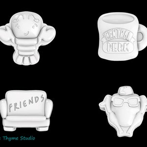 May include: Set of four white cookie cutters featuring iconic Friends TV show symbols: a lobster, a coffee mug with "Central Perk" text, a sofa with "FRIENDS" text, and a turkey wearing a chef's hat and glasses.