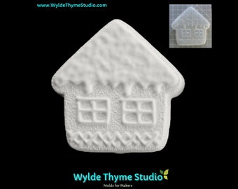 Puede incluir: Molde de plástico blanco de una pequeña casa con un techo nevado y dos ventanas. El molde está diseñado para hacer manualidades o decoraciones.