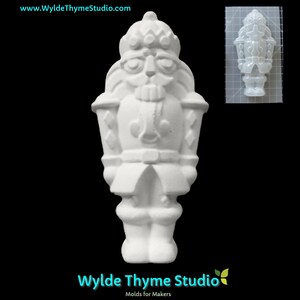 May include: White plastic mold of a nutcracker figurine. The mold is approximately 4 inches tall and features a detailed design of a traditional nutcracker with a hat, mustache, and a sword.