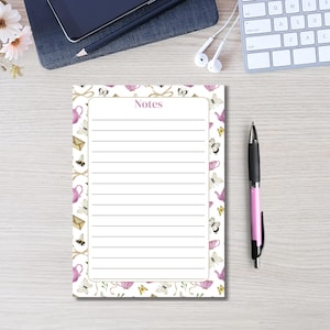 May include: A rectangular notepad with a white center featuring horizontal lines and the word Notes printed at the top. The border displays a repeating pattern of pink teapots, butterflies, bees, and envelopes on a white background.