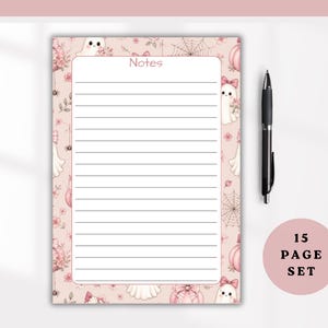 Puede incluir: Un bloc de notas rectangular con fondo rosa que presenta un patrón de fantasmas, calabazas, lazos y telarañas. El centro tiene un área blanca con líneas horizontales y la palabra Notes en la parte superior. Un bolígrafo negro está al lado.