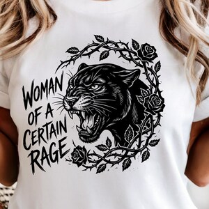 Op de afbeelding: Wit T-shirt met een zwarte panterillustratie omringd door rozen en doornen. De tekst "Woman of a Certain Rage" staat op het shirt. Een casual kledingstuk.