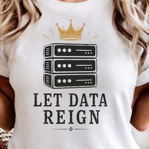 Puede incluir: Una camiseta blanca con un gráfico de una pila de tres unidades de servidor negras coronadas con una corona dorada. Debajo del gráfico, el texto "LET DATA REIGN" aparece en una fuente oscura y negrita, con un pequeño diamante centrado.
