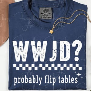 May include: Navy blue t-shirt with the text "WWJD? probably flip tables" in white. The shirt has a checkered pattern and star accents. A gold necklace with a star pendant and a brown hat are also visible.