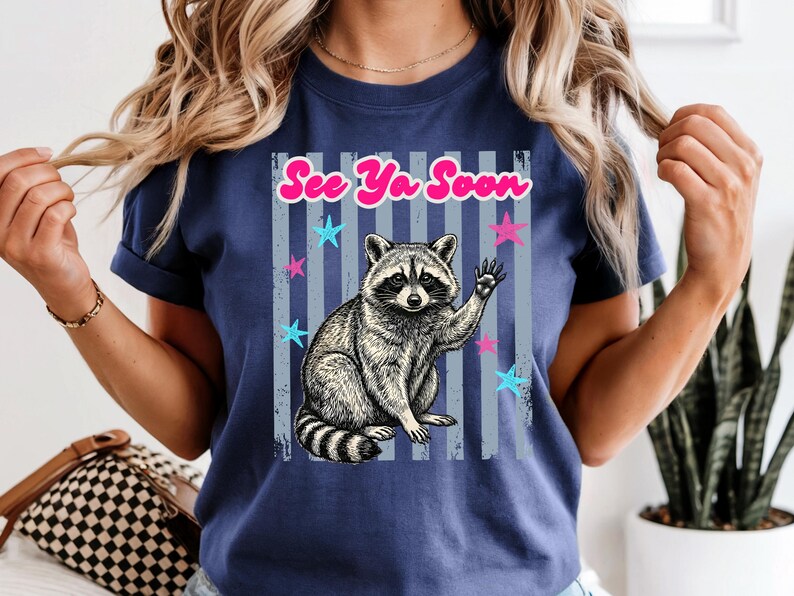 Peut inclure: T-shirt bleu marine avec un dessin de raton laveur qui salue. Le texte "See Ya Soon" est au-dessus du raton laveur, avec des &eacute;toiles et des rayures verticales. Le motif est imprim&eacute; sur un t-shirt &agrave; manches courtes.