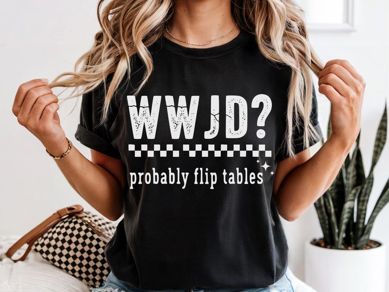 May include: Black t-shirt with the white text "WWJD?" above "probably flip tables." The design includes a checkered pattern and star accents. The shirt is a casual, comfortable style.
