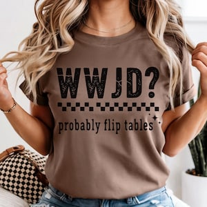 May include: A brown t-shirt with the text "WWJD? probably flip tables" in black. The shirt has a checkered pattern and star graphics. The shirt is a casual wear item.