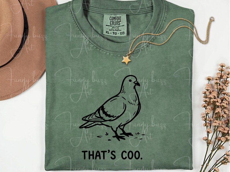 May include: Sage green t-shirt with a black graphic of a pigeon and the text "THAT'S COO." A gold necklace with a star pendant is draped over the shirt. The shirt is labeled XL-TG-EG.