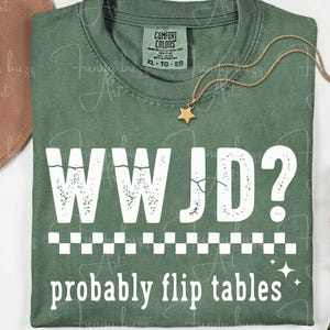 May include: Green t-shirt with the text "WWJD? probably flip tables" in white. The shirt has a crew neck and short sleeves. A gold star pendant necklace and a brown hat are also visible.