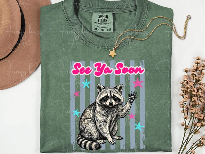 Peut inclure: T-shirt vert avec un dessin de raton laveur qui fait signe, le texte "See Ya Soon" et des &eacute;toiles. Un collier dor&eacute; avec un pendentif en forme d'&eacute;toile est pos&eacute; sur le t-shirt. Taille XL-TG-EG.