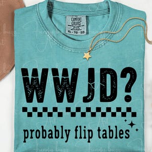 May include: A turquoise Comfort Colors t-shirt with the text "WWJD? probably flip tables" in black. A gold star pendant necklace rests on the shirt. The shirt has a crew neck and short sleeves.