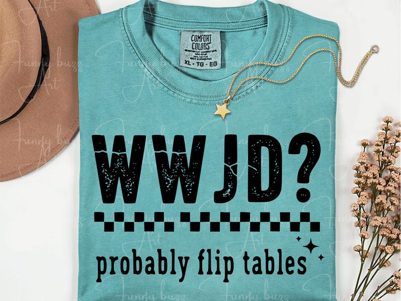 May include: A turquoise Comfort Colors t-shirt with the text "WWJD? probably flip tables" in black. A gold star pendant necklace rests on the shirt. The shirt has a crew neck and short sleeves.