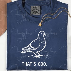 May include: Navy blue t-shirt with a white outline drawing of a pigeon and the text "THAT'S COO." A gold star pendant hangs on a gold chain. The shirt is labeled XL-TG-EG.