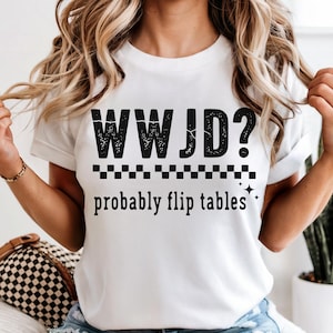 May include: White t-shirt with the text "WWJD? probably flip tables" in black. The text is above a checkered pattern and two small star graphics. The shirt is a casual, everyday wear item.