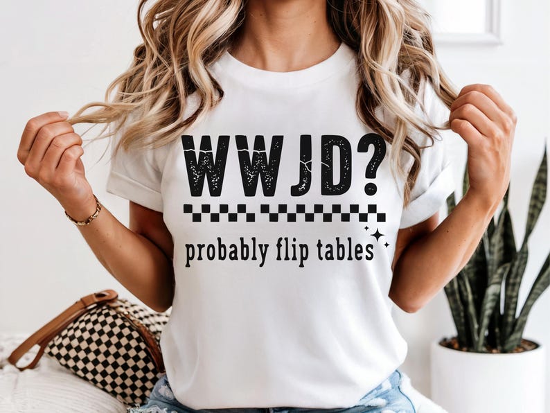 May include: White t-shirt with the text "WWJD? probably flip tables" in black. The text is above a checkered pattern and two small star graphics. The shirt is a casual, everyday wear item.