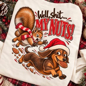 May include: A white sweatshirt featuring a graphic of a brown squirrel wearing a red and white striped scarf and a brown dachshund wearing a red Santa hat. The text reads Well, shit... MY NUTS! with scattered brown nut pieces.