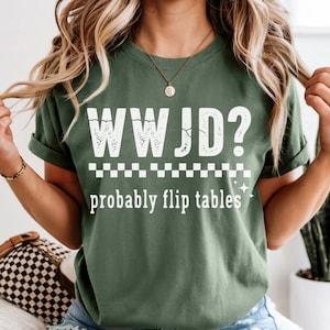 May include: Olive green t-shirt with the text "WWJD? probably flip tables" in white. The shirt has a distressed font and a checkered pattern. The shirt is a casual wear item.