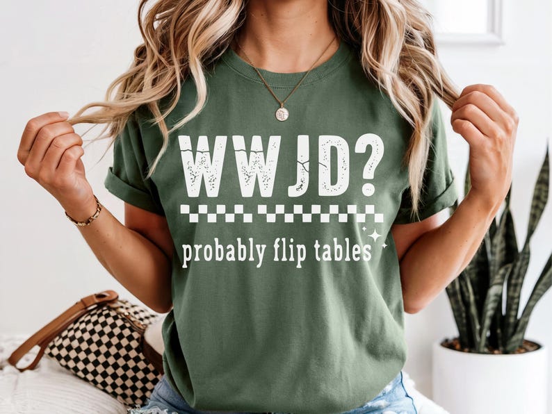 May include: Olive green t-shirt with the text "WWJD? probably flip tables" in white. The shirt has a distressed font and a checkered pattern. The shirt is a casual wear item.