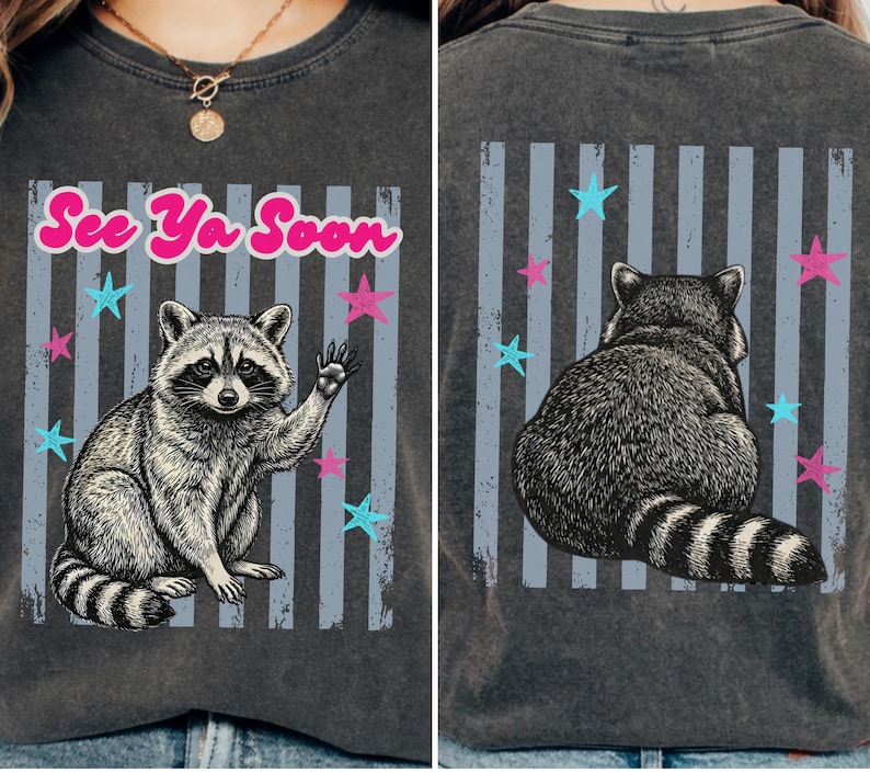 Peut inclure: T-shirt gris fonc&eacute; avec une illustration de raton laveur. Le devant montre un raton laveur qui salue avec le texte "See Ya Soon" en rose. Le dos affiche le dos du raton laveur. Des &eacute;toiles bleues et roses et des rayures verticales compl&egrave;tent le design.